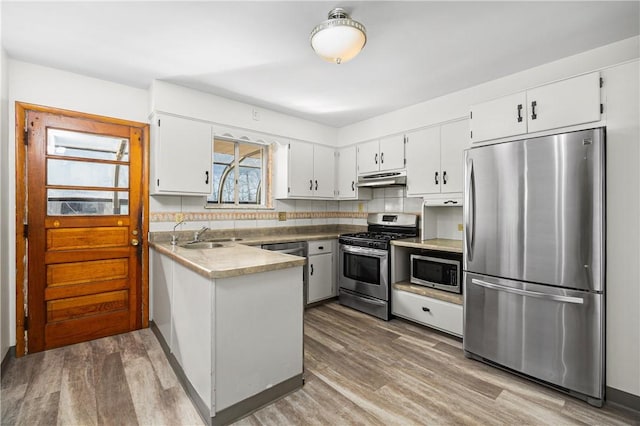 kitchen featuring under cabinet range hood, a sink, light wood-style floors, appliances with stainless steel finishes, and a peninsula