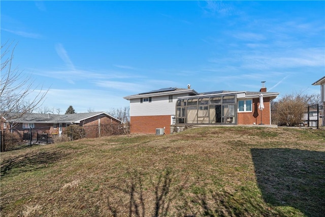 back of property with a yard, brick siding, solar panels, and a sunroom