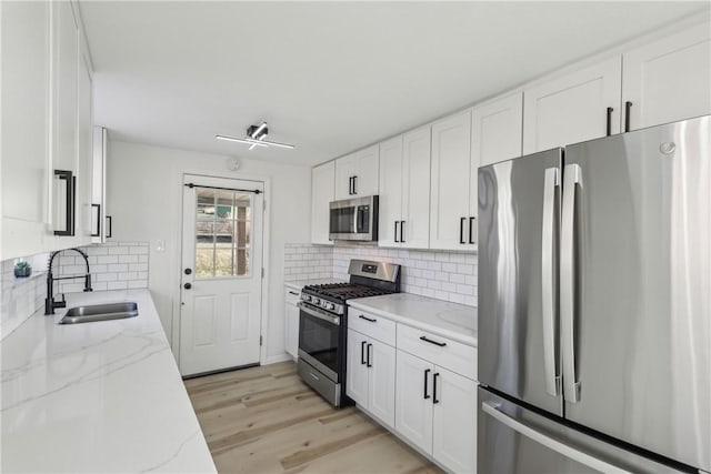 kitchen with light stone counters, appliances with stainless steel finishes, white cabinetry, and a sink