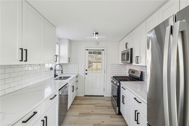 kitchen with a sink, stainless steel appliances, white cabinets, light wood finished floors, and light stone countertops