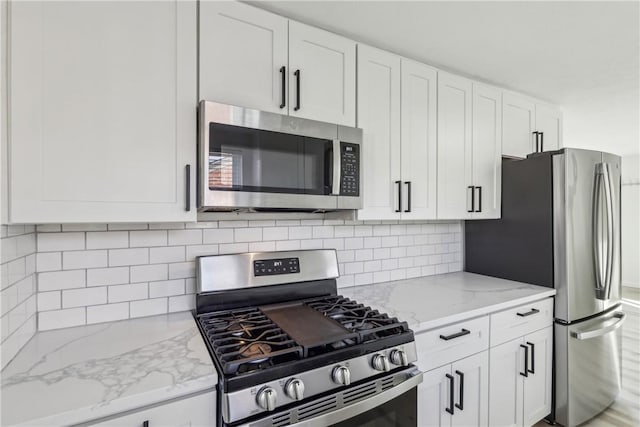 kitchen with stainless steel appliances, light stone countertops, tasteful backsplash, and white cabinetry