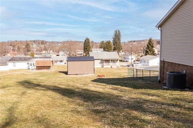 view of yard featuring a storage unit, fence, a residential view, an outdoor structure, and central AC unit