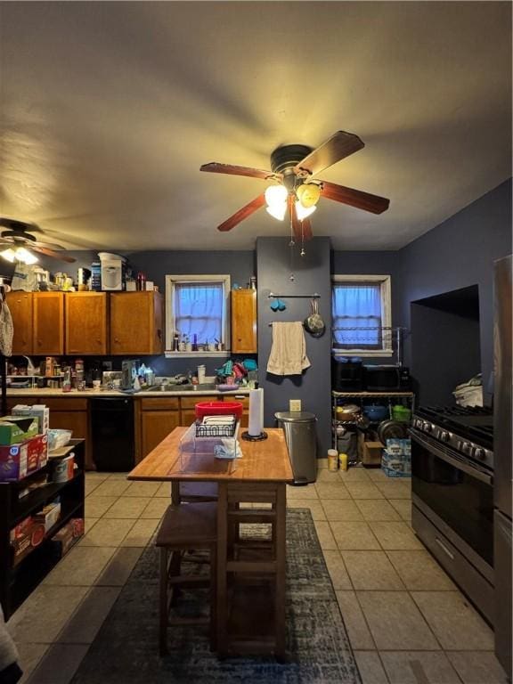 kitchen with stainless steel gas range oven, black dishwasher, light tile patterned floors, brown cabinets, and a ceiling fan