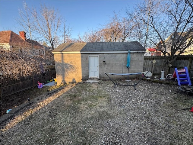 back of house featuring an outbuilding, concrete block siding, a fenced backyard, and roof with shingles