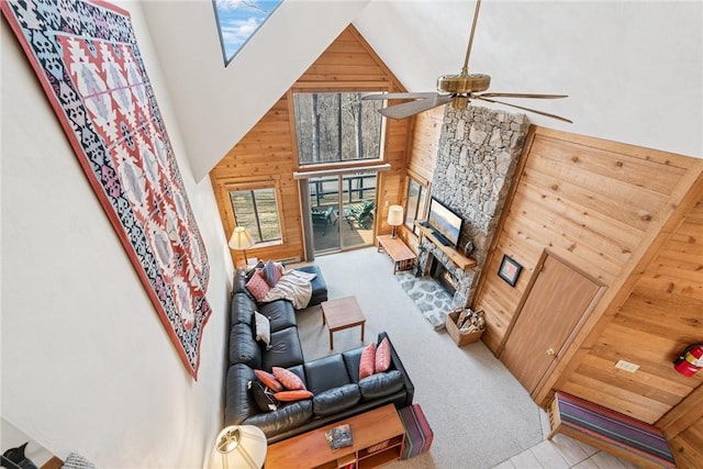 living area with high vaulted ceiling, wooden walls, carpet, a fireplace, and ceiling fan