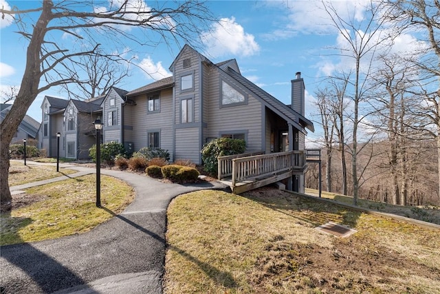 view of home's exterior with aphalt driveway, a yard, a deck, and a chimney