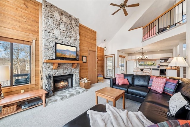 carpeted living room with wooden walls, ceiling fan with notable chandelier, a fireplace, and plenty of natural light