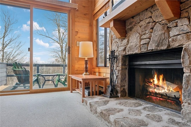 unfurnished room featuring a stone fireplace, carpet flooring, and wooden walls