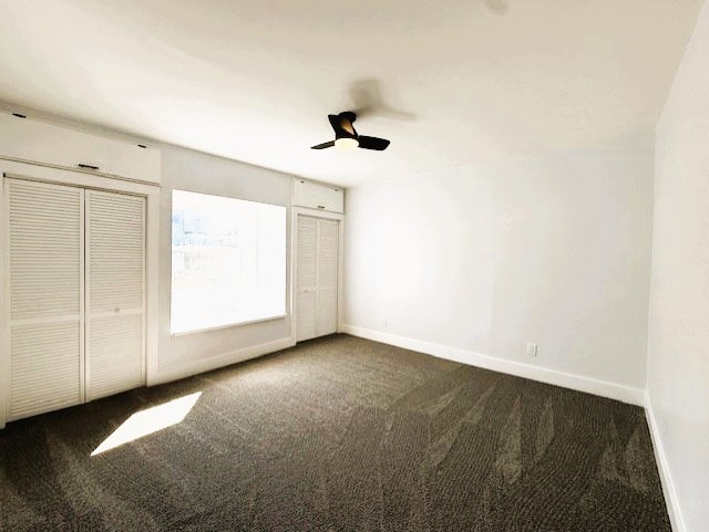 unfurnished bedroom featuring baseboards, dark carpet, and ceiling fan