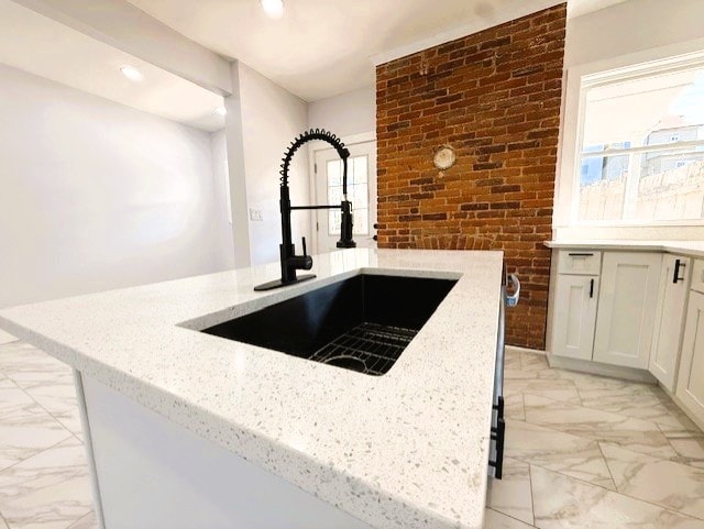 kitchen featuring light stone counters, brick wall, recessed lighting, a sink, and marble finish floor