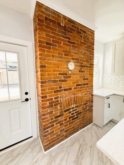 interior space with plenty of natural light, backsplash, marble finish floor, and brick wall