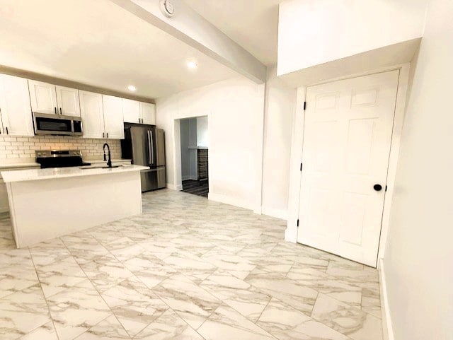 kitchen with beamed ceiling, marble finish floor, a sink, appliances with stainless steel finishes, and light countertops