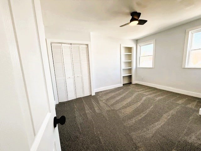 unfurnished bedroom featuring a ceiling fan, baseboards, dark colored carpet, and multiple closets