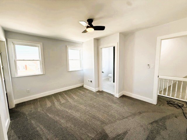 unfurnished bedroom with ensuite bath, a ceiling fan, baseboards, and dark colored carpet