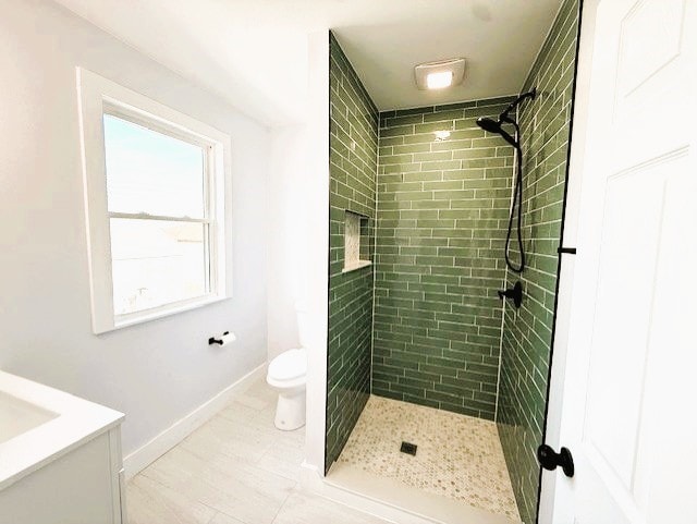 full bathroom with toilet, tiled shower, vanity, and baseboards