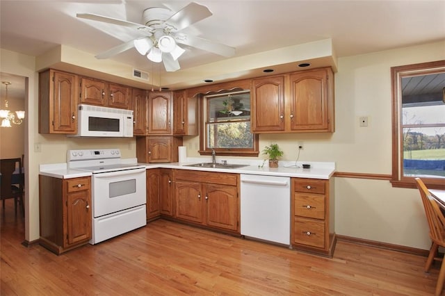 kitchen with white appliances, light wood-style flooring, brown cabinetry, and a sink