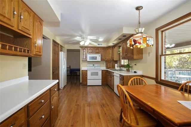 kitchen featuring white appliances, wood finished floors, a sink, light countertops, and brown cabinets