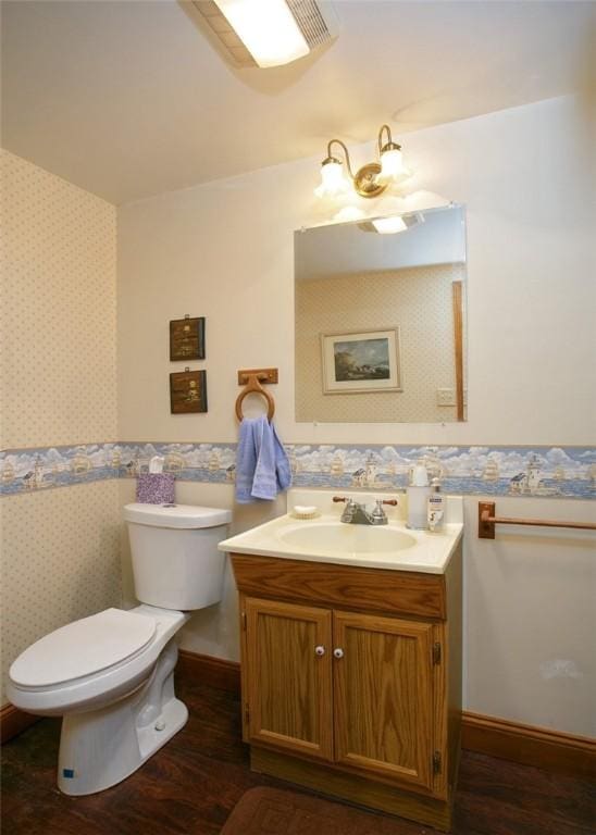 bathroom featuring toilet, wood finished floors, wallpapered walls, baseboards, and vanity