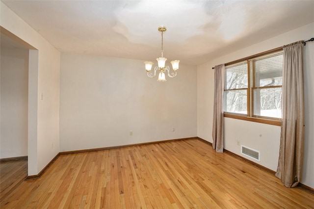 spare room featuring a chandelier, visible vents, light wood-type flooring, and baseboards