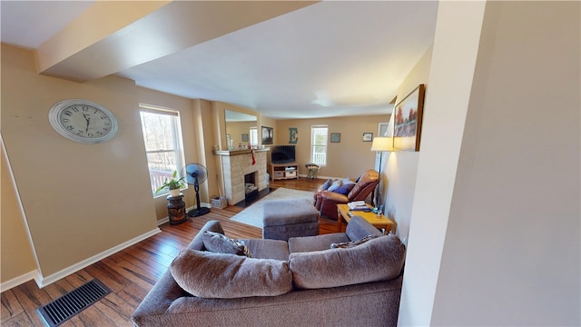 living area featuring hardwood / wood-style floors, a tiled fireplace, baseboards, and visible vents