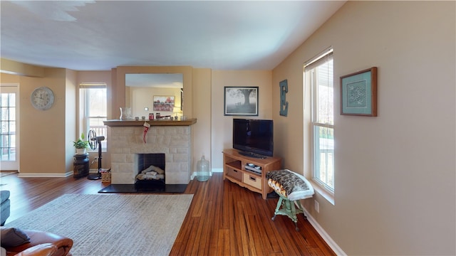 living room featuring a stone fireplace, dark wood-style floors, and baseboards