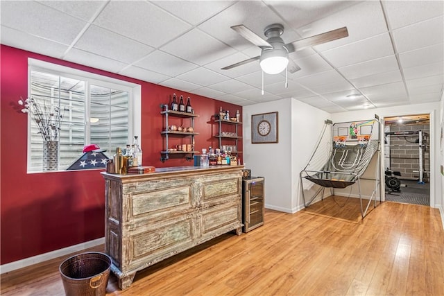 bar with light wood-style flooring, a paneled ceiling, a dry bar, and a ceiling fan