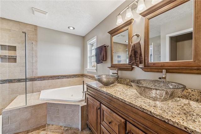 bathroom with a textured ceiling, a jetted tub, visible vents, and a sink