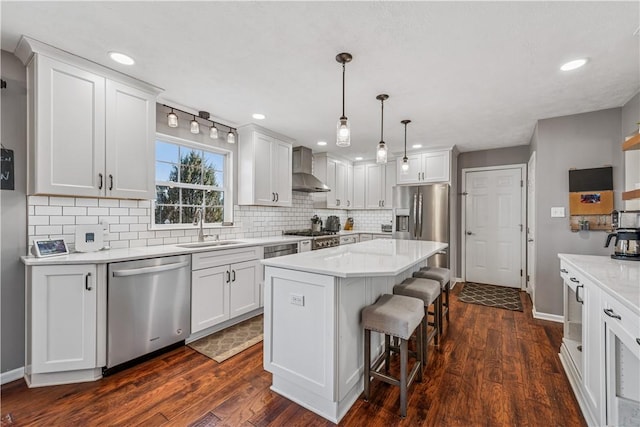 kitchen with a breakfast bar area, appliances with stainless steel finishes, dark wood-style floors, wall chimney exhaust hood, and a sink