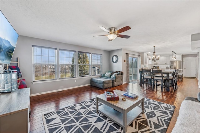 living area featuring baseboards, dark wood-style flooring, and ceiling fan with notable chandelier