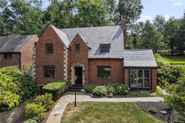 english style home with brick siding, a high end roof, and a chimney