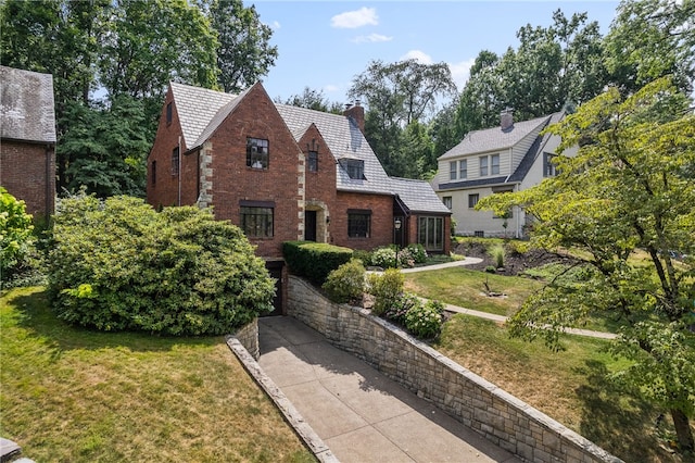 english style home with brick siding, a chimney, and a front lawn