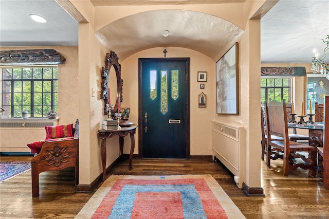 entryway featuring baseboards, an inviting chandelier, wood finished floors, and a textured wall