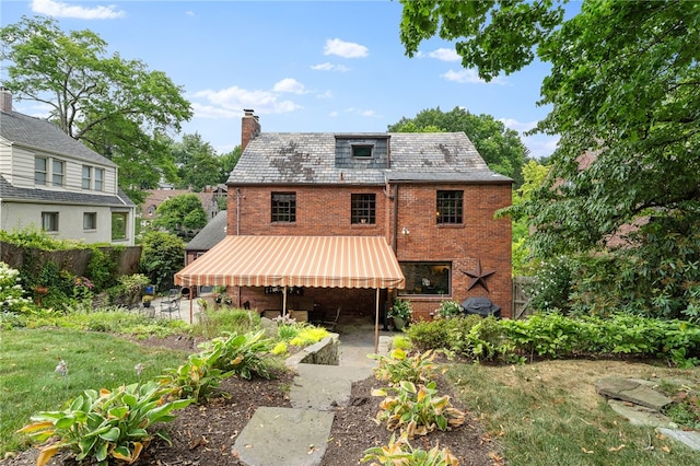 rear view of house featuring brick siding, a high end roof, a chimney, and a patio