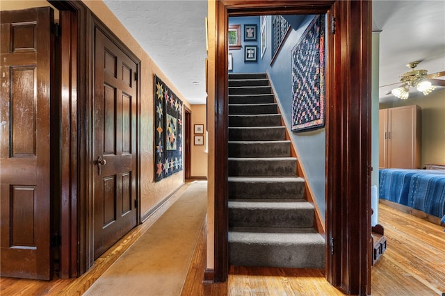 stairway featuring baseboards, wood finished floors, a textured ceiling, and ceiling fan