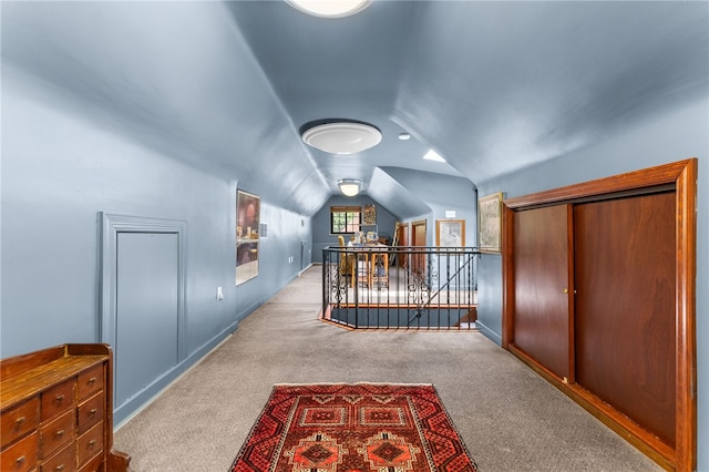 hallway featuring vaulted ceiling, an upstairs landing, baseboards, and carpet floors