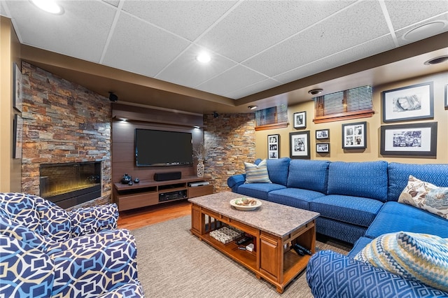 living area with a drop ceiling, a stone fireplace, and light wood-style floors