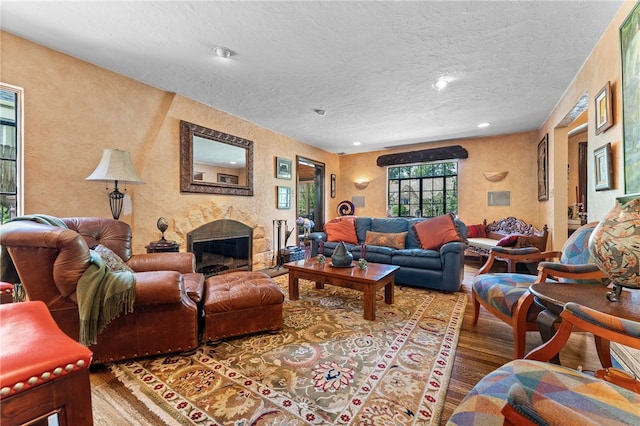 living area with a glass covered fireplace, a textured ceiling, wood finished floors, and a textured wall