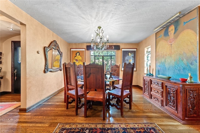 dining space with wood finished floors, baseboards, a textured ceiling, a textured wall, and a chandelier