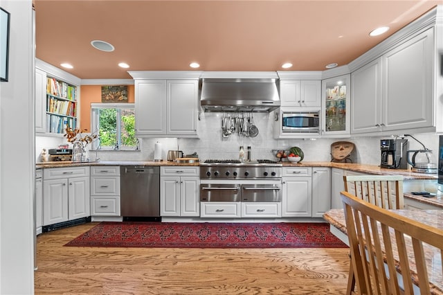 kitchen with backsplash, glass insert cabinets, wall chimney range hood, white cabinets, and stainless steel appliances