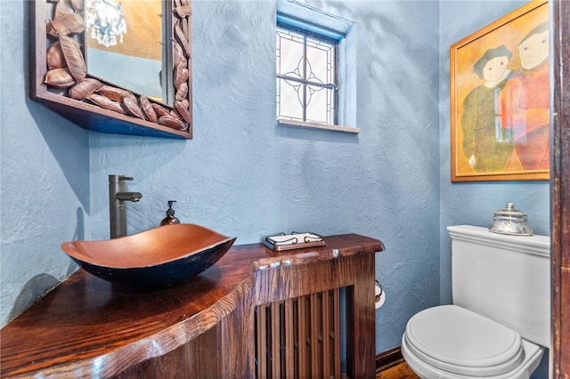 half bath featuring toilet, a textured wall, and a sink