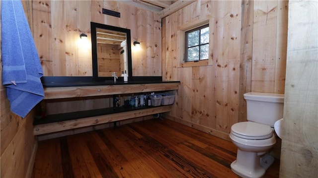 half bathroom with toilet, wood finished floors, vanity, and wood walls