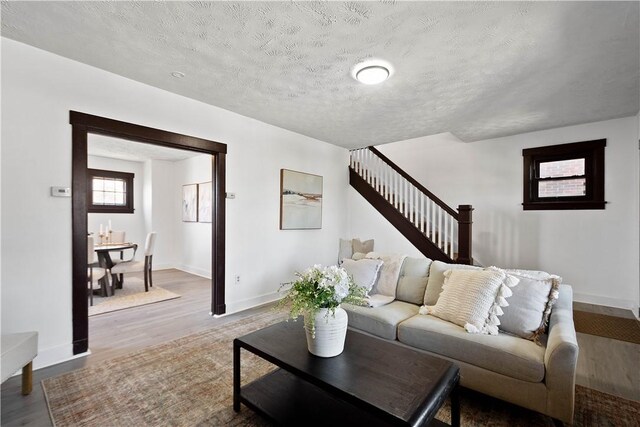 living area with stairway, baseboards, a textured ceiling, and wood finished floors