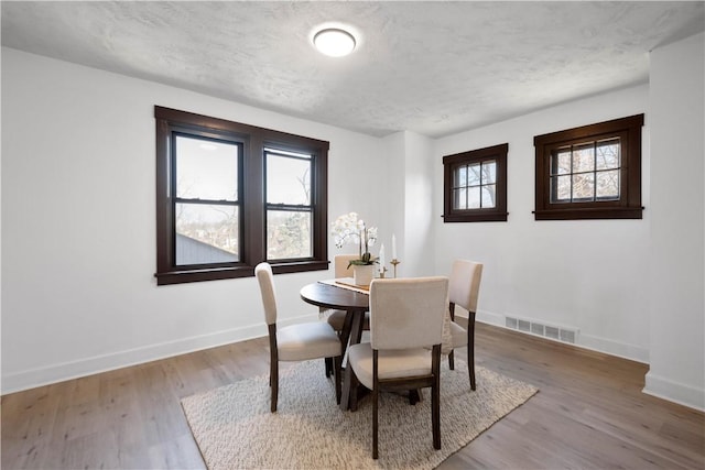 dining room featuring baseboards, wood finished floors, visible vents, and a textured ceiling