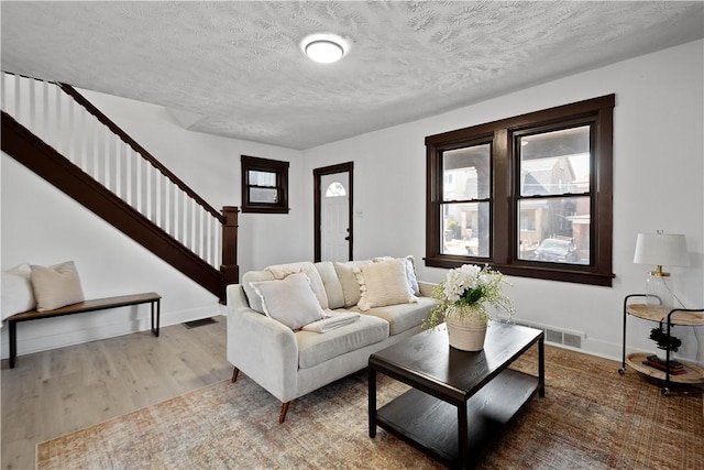 living area with visible vents, baseboards, stairway, wood finished floors, and a textured ceiling