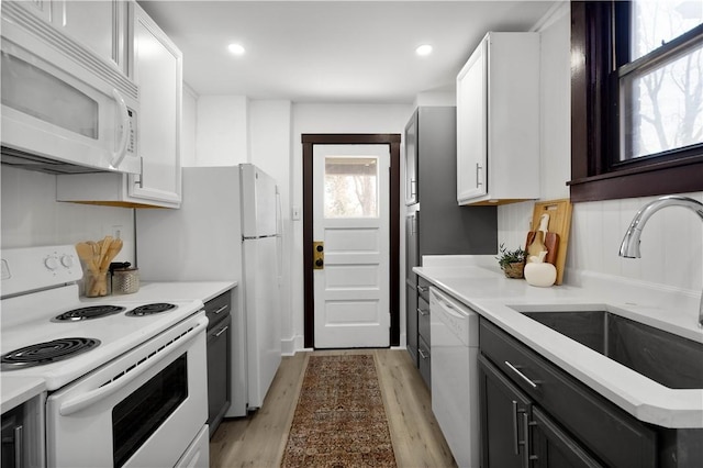 kitchen featuring white appliances, light wood-type flooring, light countertops, and a sink