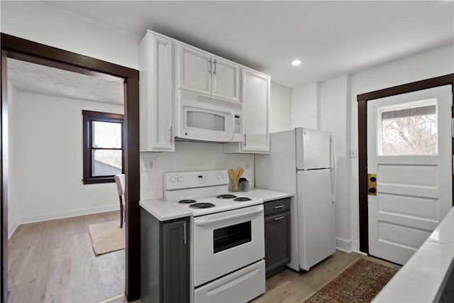 kitchen with light wood finished floors, white appliances, white cabinets, and light countertops