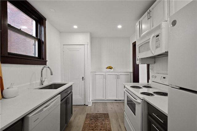 kitchen with light wood-type flooring, light countertops, white cabinets, white appliances, and a sink