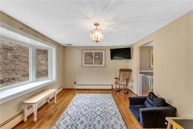 living area featuring visible vents, light wood-style flooring, a baseboard heating unit, and an inviting chandelier