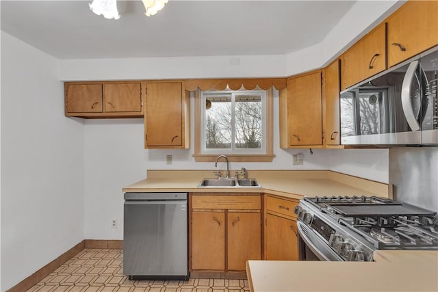 kitchen featuring baseboards, light countertops, appliances with stainless steel finishes, brown cabinetry, and a sink