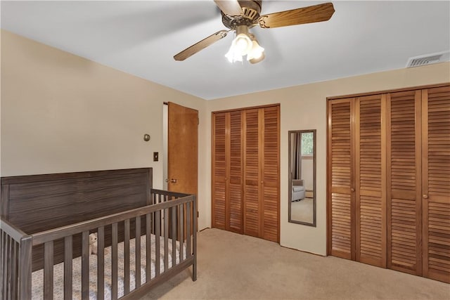 bedroom featuring visible vents, two closets, light colored carpet, and a ceiling fan